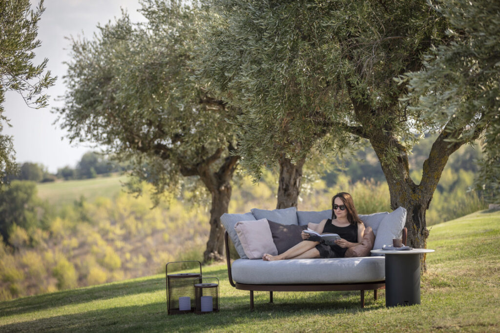 Grüne Oasen – Frau liest auf Sofa unter Olivenbäumen